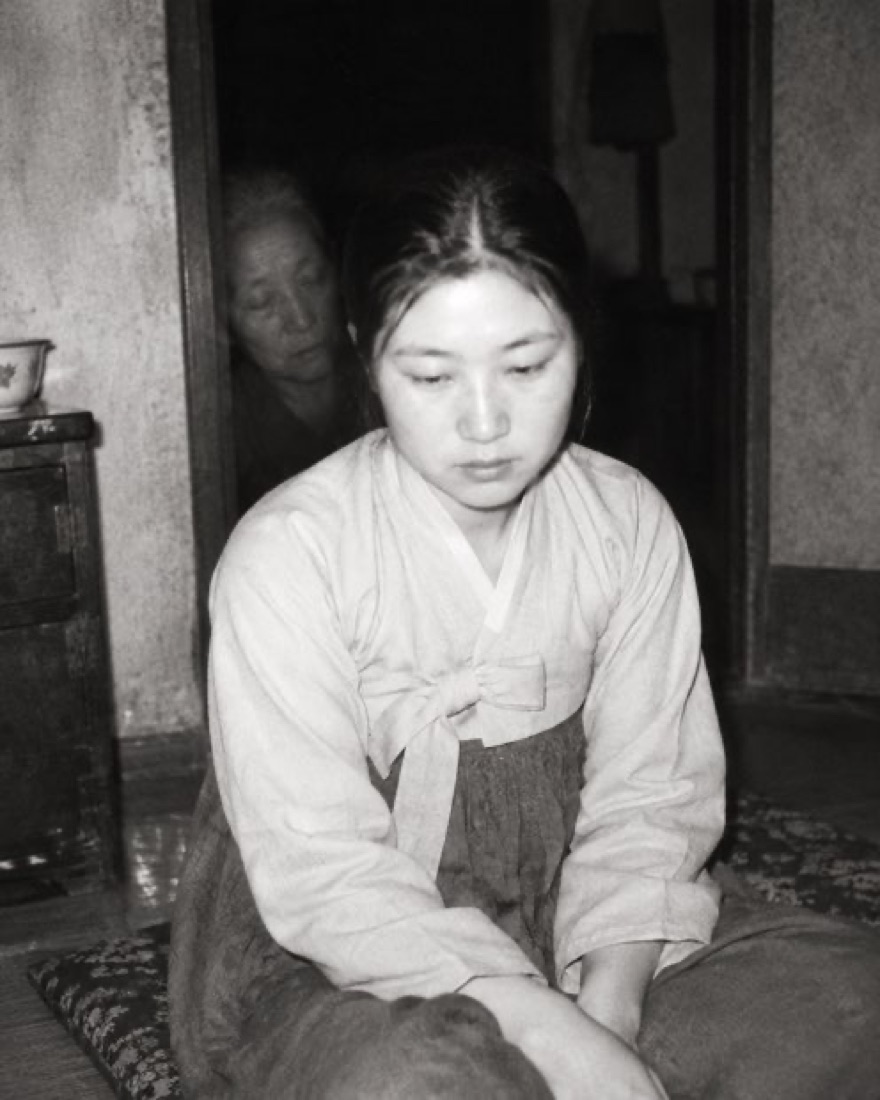 방에 앉은 여자, 그 어깨 뒤 문간의 희미한 얼굴